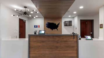 A reception area with a wooden reception desk, a map of the USA on the wall, a ceiling fan, and a TV mounted on the wall.