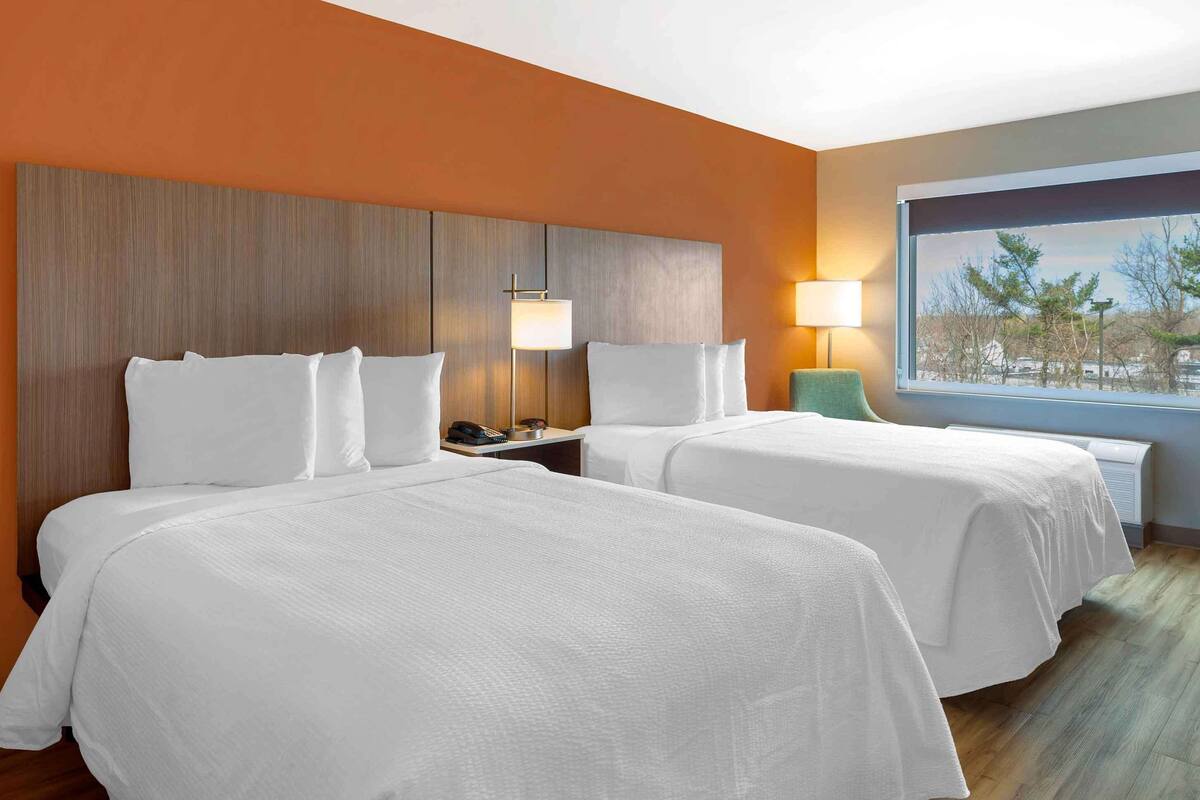 Une chambre d’hôtel avec deux lits, une table de chevet, une lampe et une fenêtre donnant sur un beau paysage.