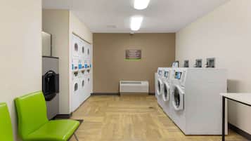 A hotel laundry room with a washing machine, dryer, and a folding station.