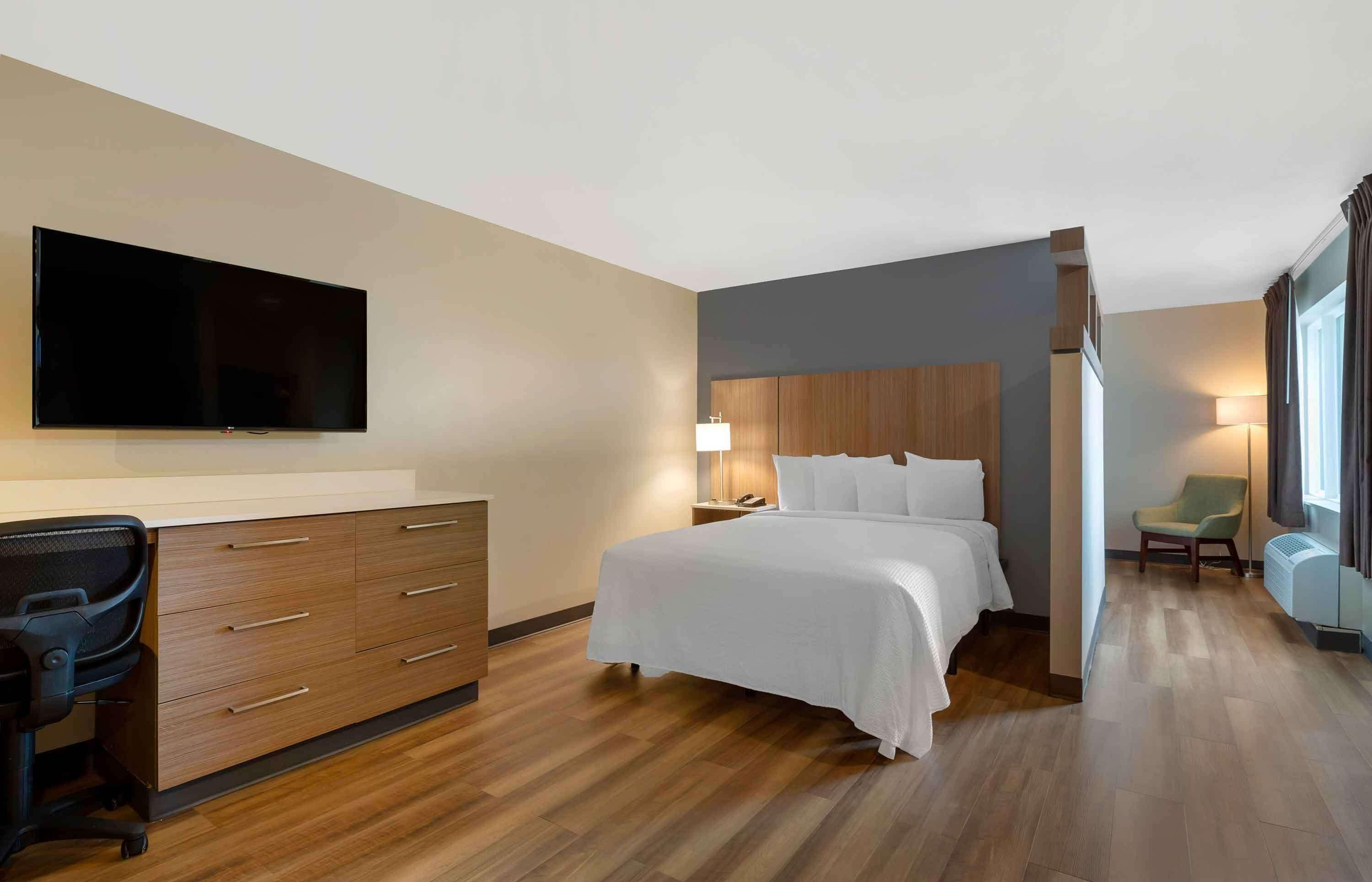 A hotel room with a bed, a desk with a chair, a TV, and a lamp.
