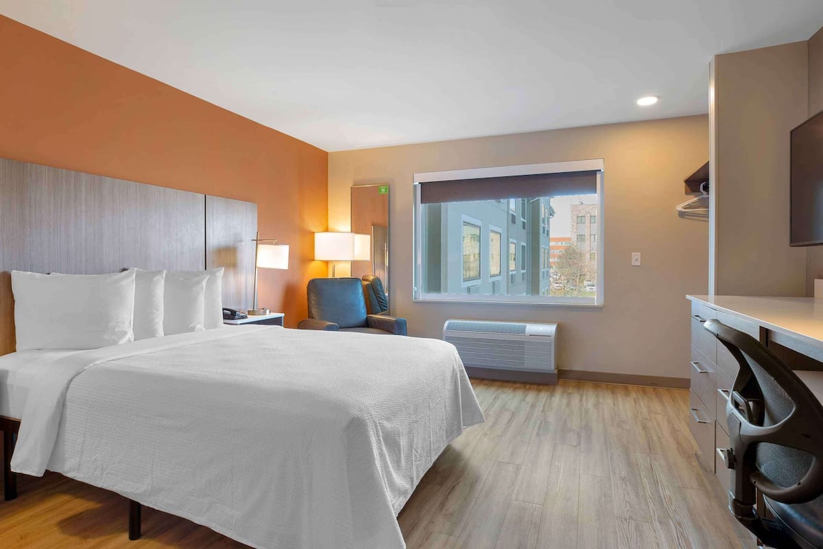 Une chambre d’hôtel avec un grand lit, un bureau, une chaise, une télévision, une fenêtre et un radiateur.