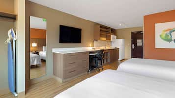Habitación de hotel con dos camas, un escritorio con silla, televisor de pantalla plana, microondas y refrigerador.