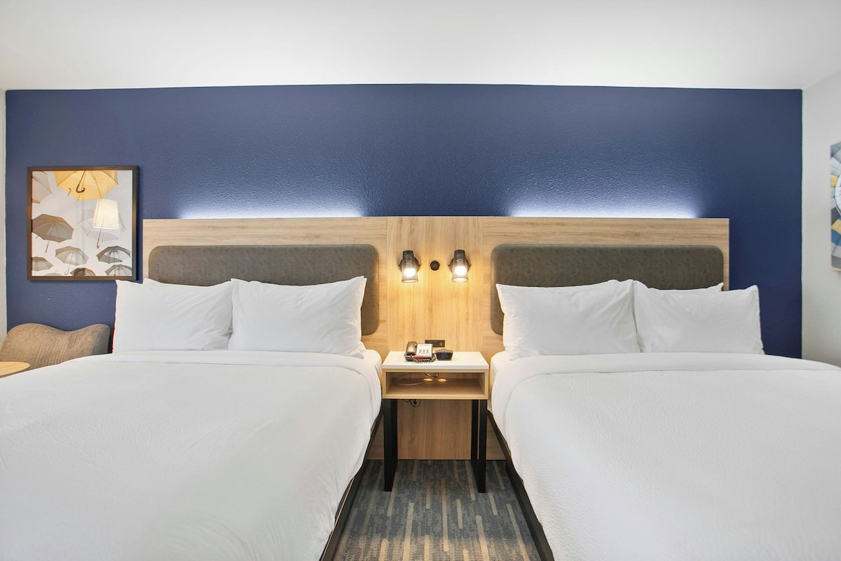 A hotel room with two beds, a wooden headboard, bedside tables with lamps, and a wall-mounted artwork.