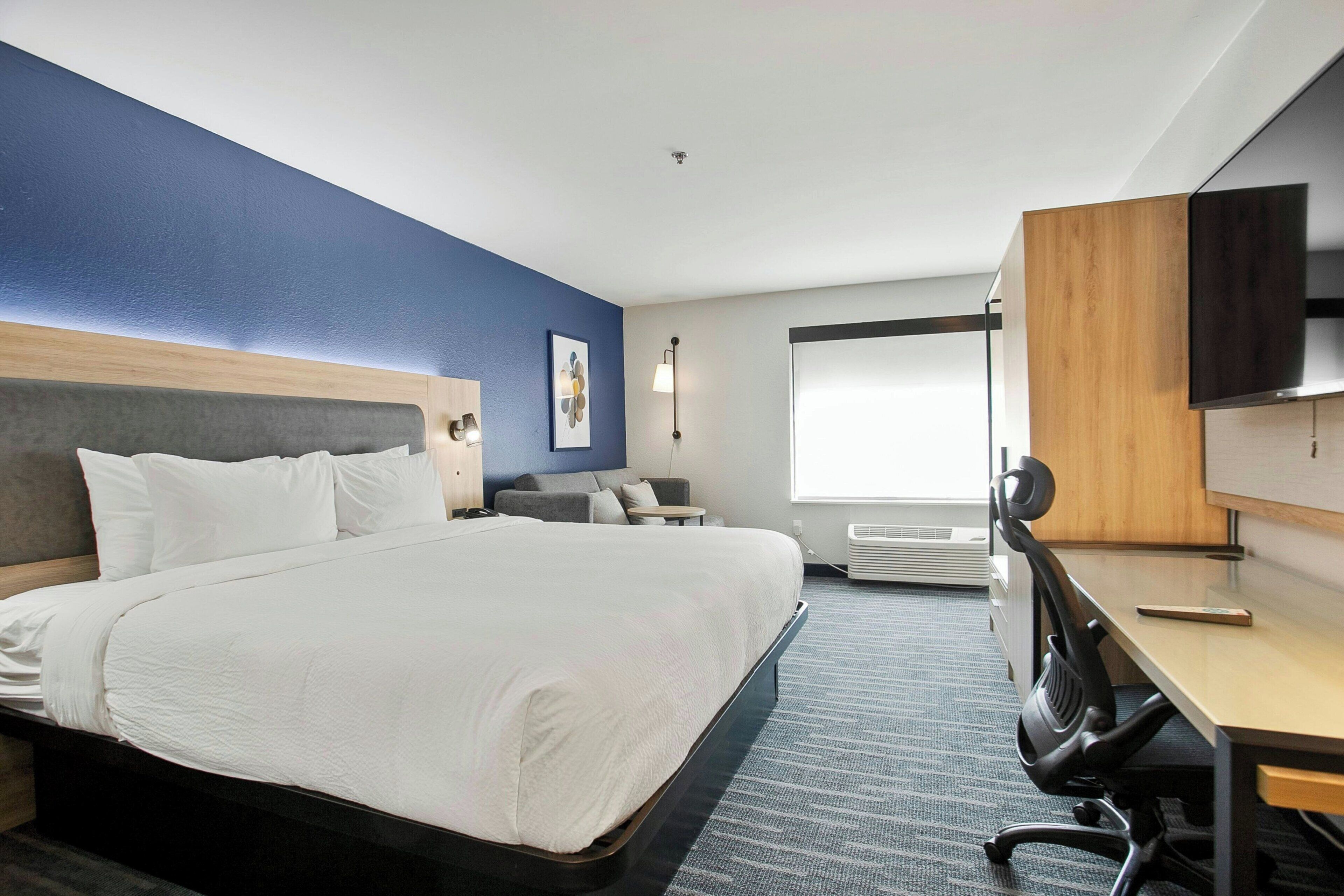 Una habitación de hotel con una cama grande, un escritorio, una silla, un televisor y una ventana.