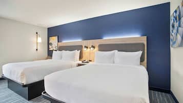 Habitación de hotel con dos camas, una mesita de noche, una lámpara y un cuadro en la pared.