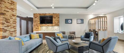 A modern living room with a sofa, armchairs, a coffee table, and a TV mounted on a brick wall.
