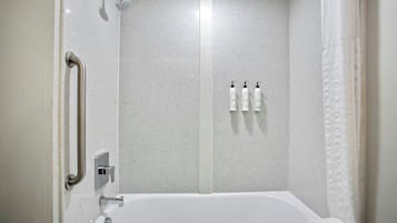 Un baño con una bañera blanca, una ducha con cabezal de ducha de mano y una barra de apoyo.