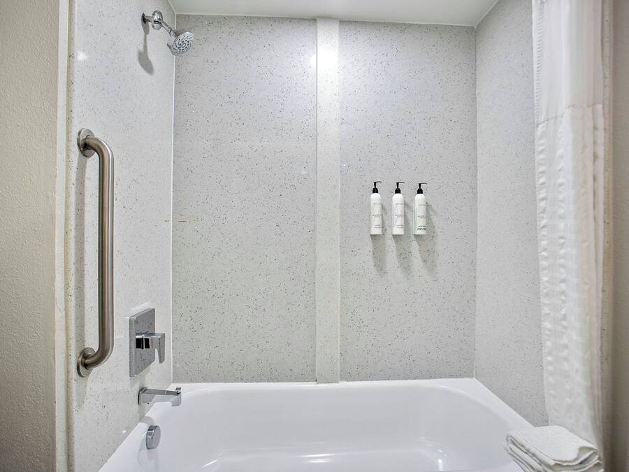 Un baño con una bañera blanca, una ducha con cabezal de ducha de mano y una barra de apoyo.