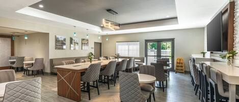 Un comedor moderno con una isla central, diversas opciones de asientos y un gran ventanal que proporciona luz natural.