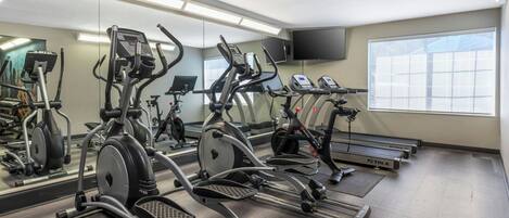 A gym with multiple cardio machines, a large mirror, and a TV on the wall.
