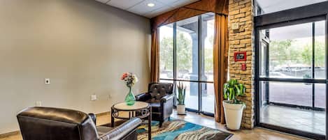 A lobby with leather chairs, a small table with a vase, a patterned rug, and a large window with a view of the parking lot.