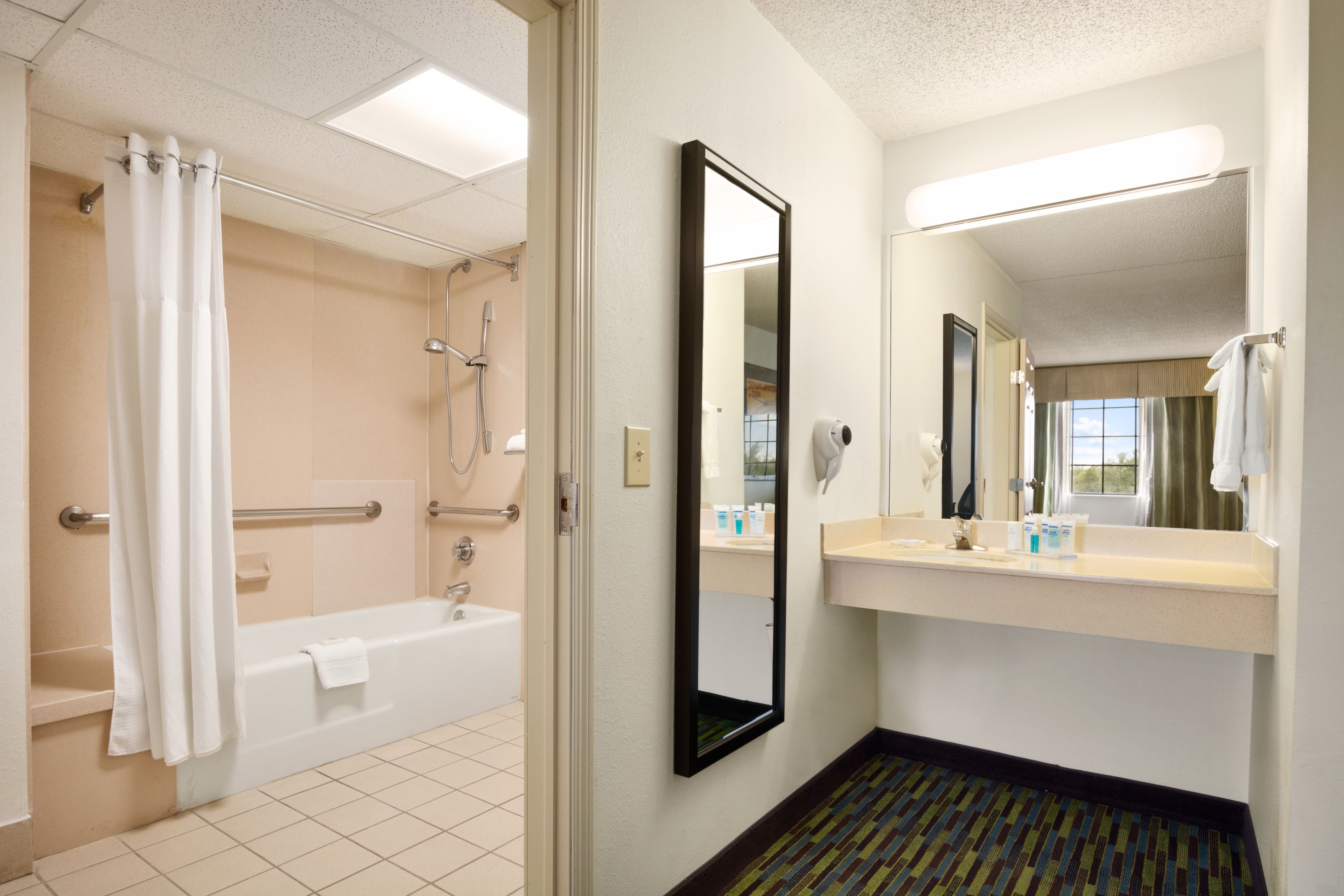 A hotel bathroom with a bathtub, shower, and a large mirror.