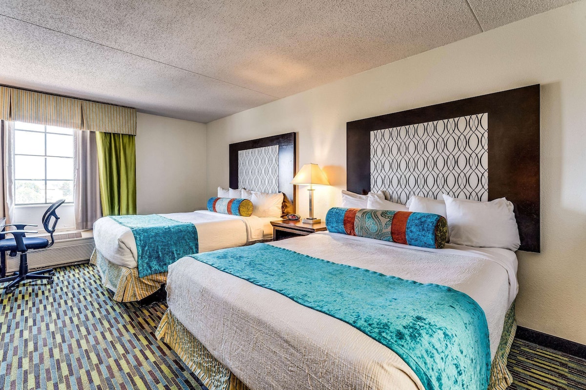 A hotel room with two beds, a desk, a chair, and a window with curtains.