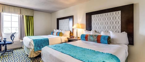 Habitación de hotel con dos camas, un escritorio, una silla y un ventanal con cortinas.
