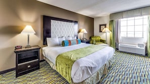 A hotel room with a large bed, two bedside tables, a wall-mounted heater, and a window with curtains. - Wyndham Garden Wichita Downtown (Wichita)