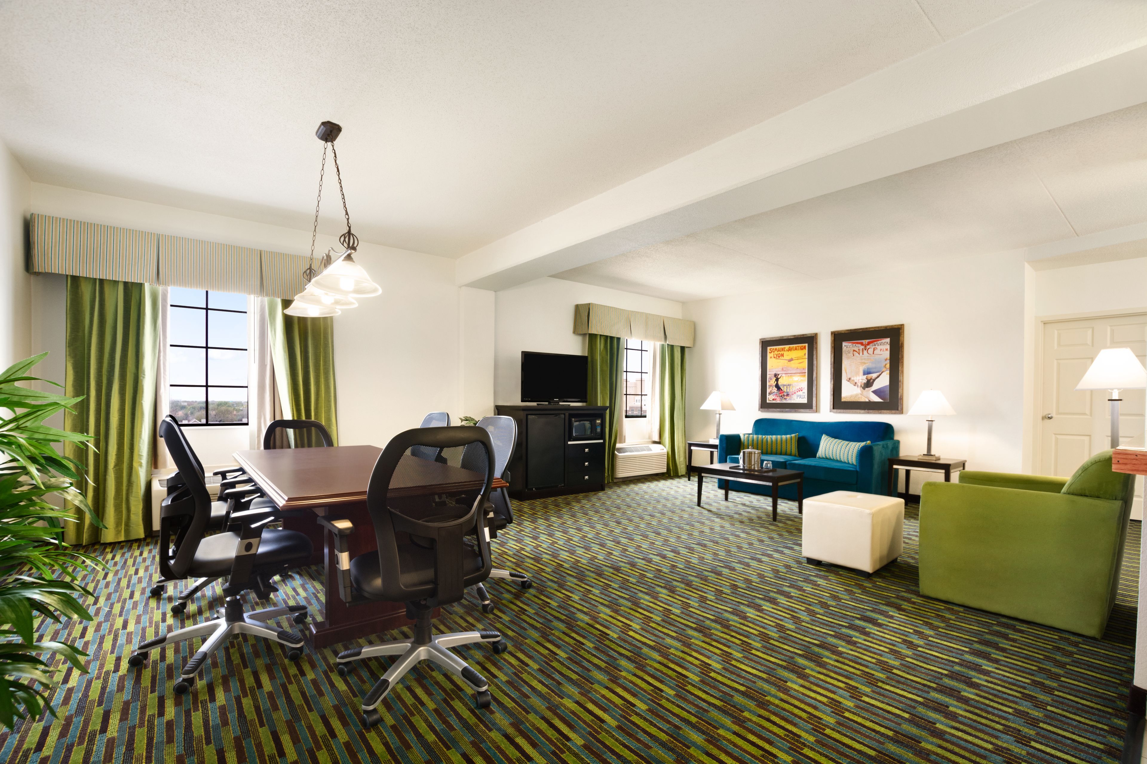 A hotel room with a dining area, a sofa, a TV, and a lamp.