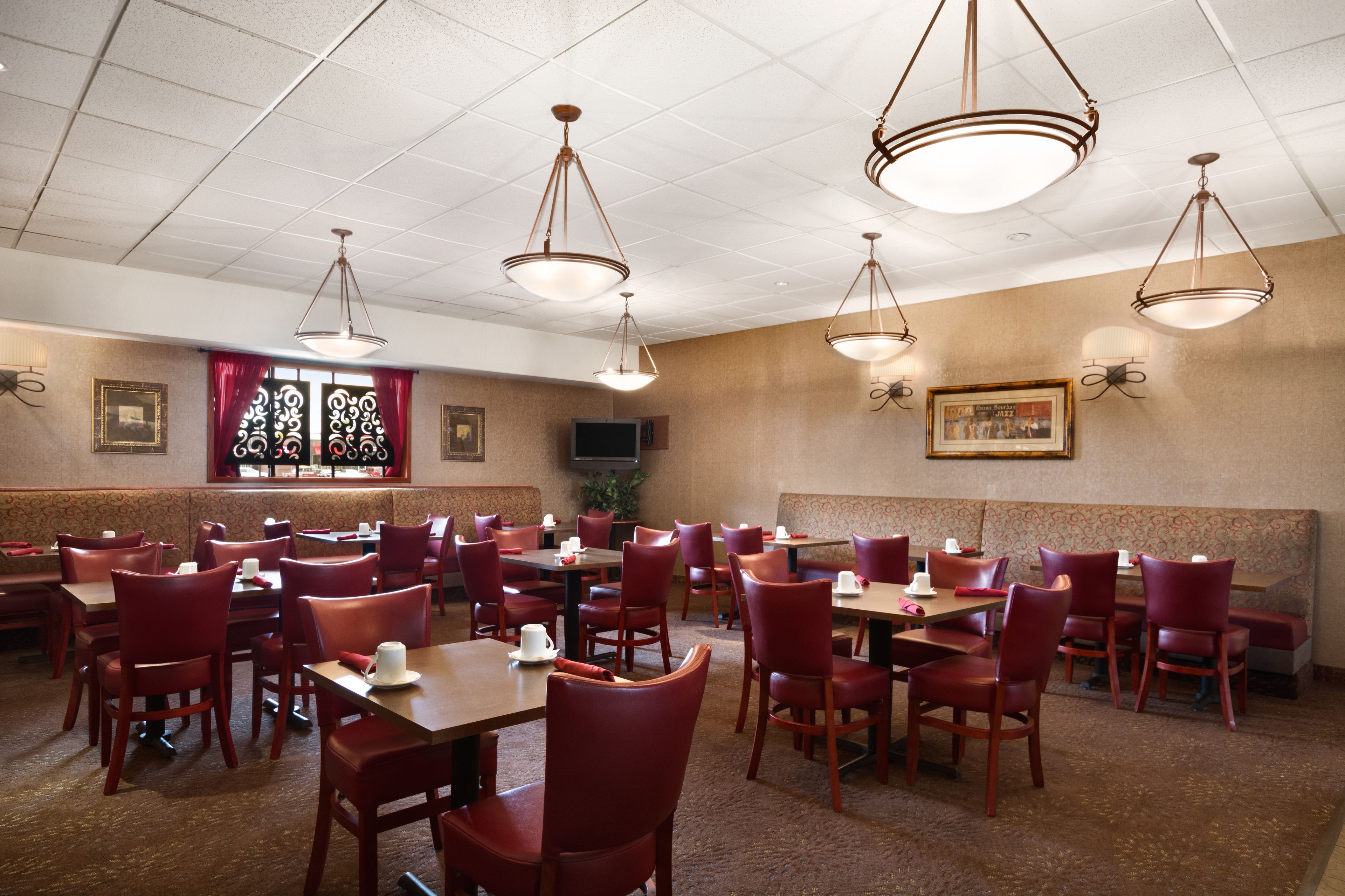 A spacious dining area with multiple tables and chairs, ceiling lights, and wall-mounted artwork.