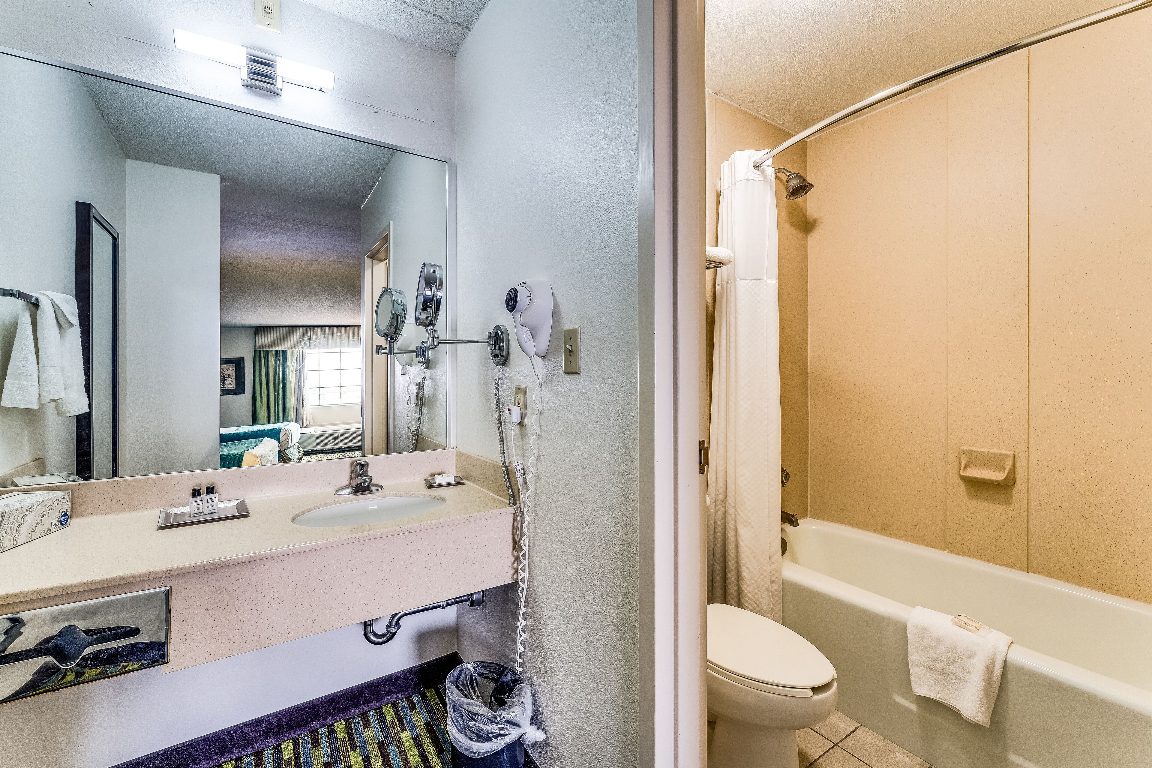 A bathroom with a sink, mirror, hairdryer, and a bathtub.