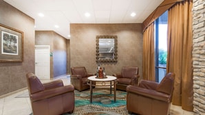 A lobby with leather chairs, a round table, a patterned rug, a mirror, and a door. - Wyndham Garden Wichita Downtown (Wichita)