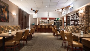 A restaurant with booths and tables, a bar area, and a patterned carpet. - Wyndham Garden Wichita Downtown (Wichita)