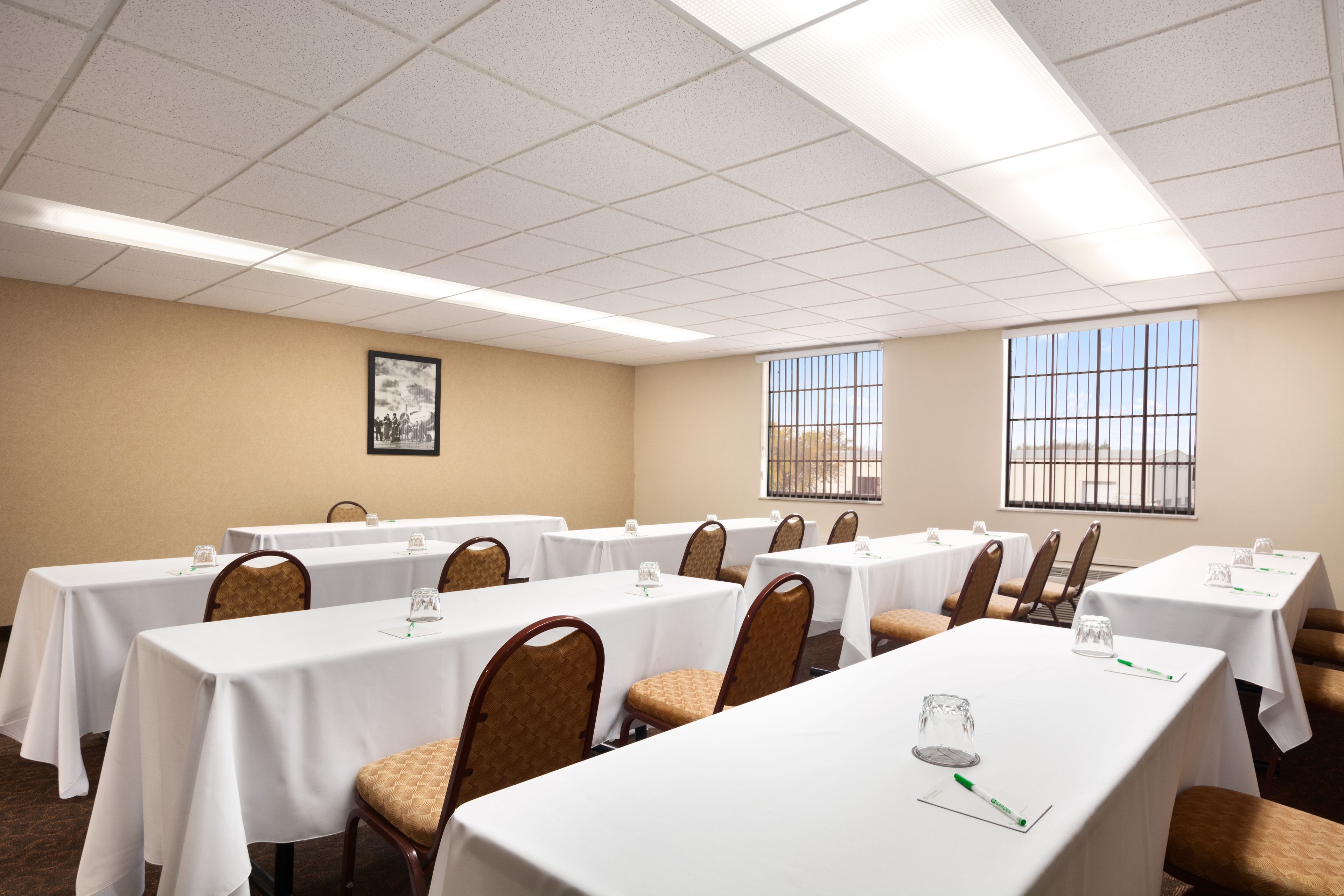 A conference room with multiple tables and chairs, large windows, and a framed picture on the wall.