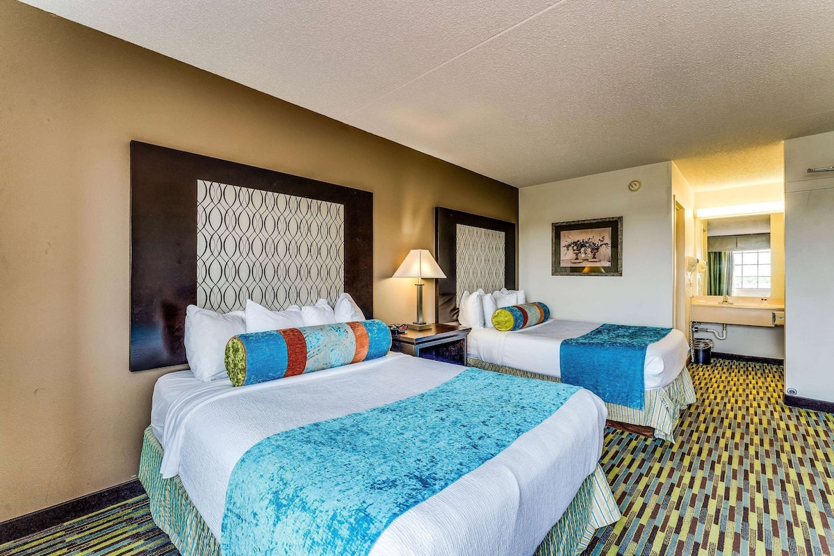 A hotel room with two beds, a nightstand, a lamp, a framed picture, and a patterned floor.