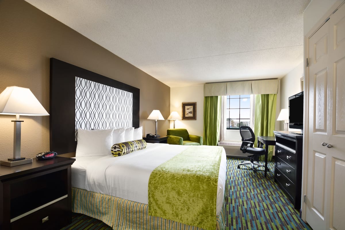 A hotel room with a bed, two bedside tables, a desk with a chair, a television, and a window with curtains.