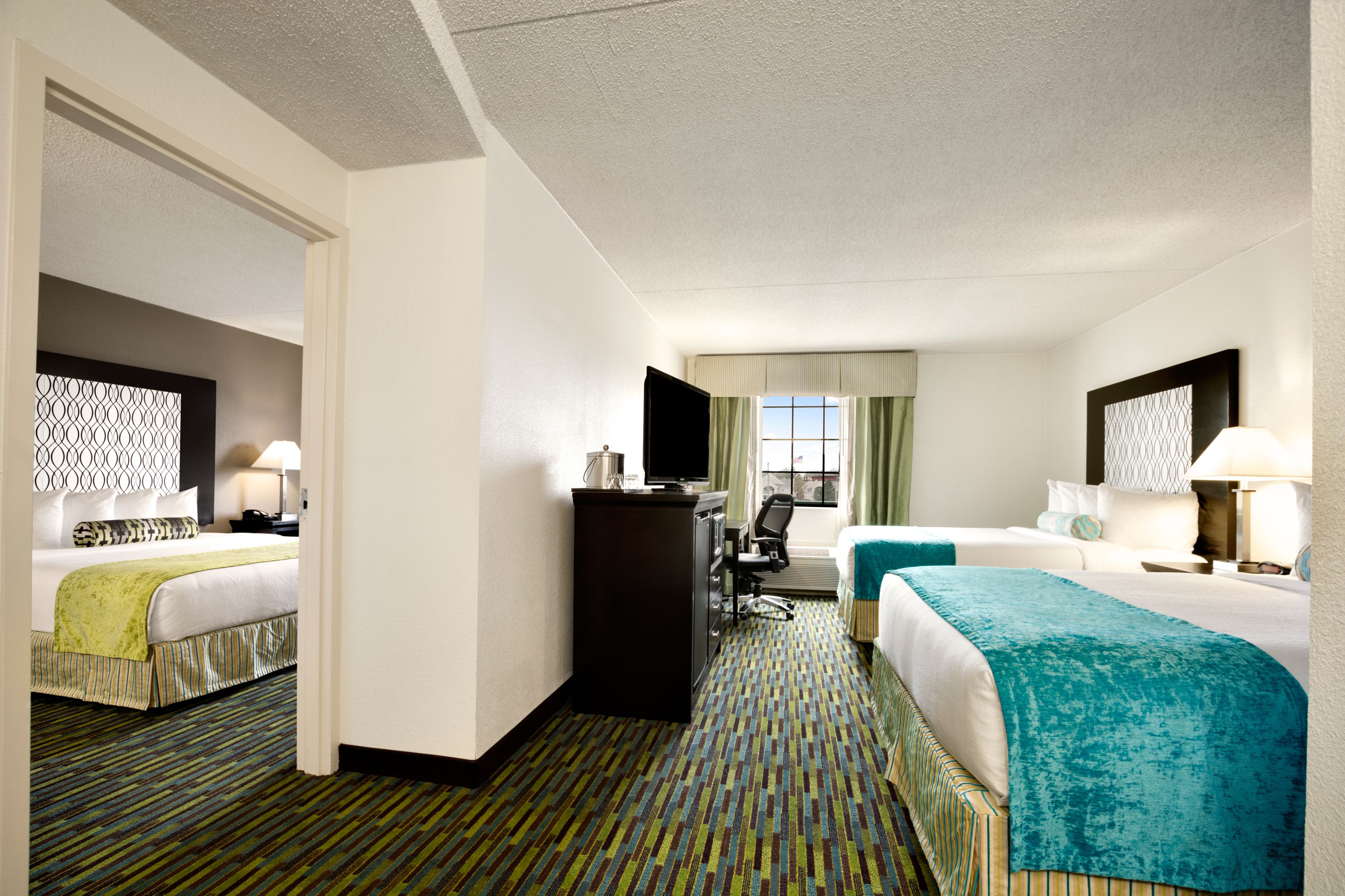 Quarto de hotel com duas camas, uma escrivaninha com computador e televisão.