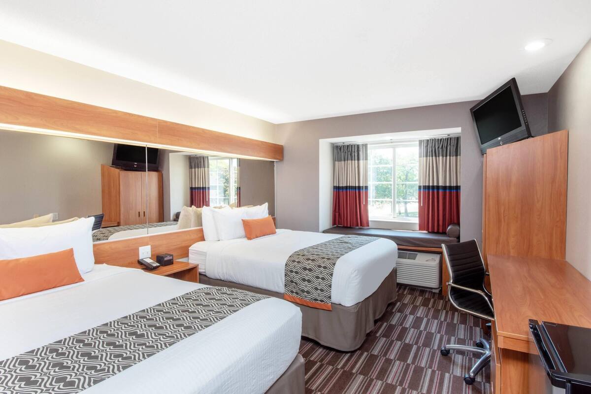 Hotellihuone, jossa on kaksi sänkyä, työpöytä, tuoli, televisio ja ikkuna, jossa on verhot.