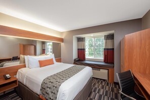 A hotel room with a large bed, a desk, a chair, a wardrobe, and a window with curtains.
