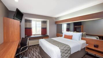 A hotel room with a bed, a desk, a chair, a television, a window with curtains, and a built-in shelf.