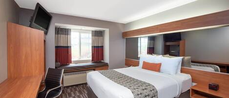 A hotel room with a bed, a desk, a chair, a television, a window with curtains, and a built-in shelf.