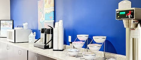 A hotel lobby with a blue wall, a coffee machine, a microwave, and a painting.