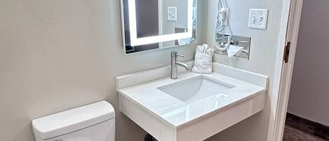 A bathroom with a white toilet, a white sink with a mirror above it, and a hairdryer on the wall.
