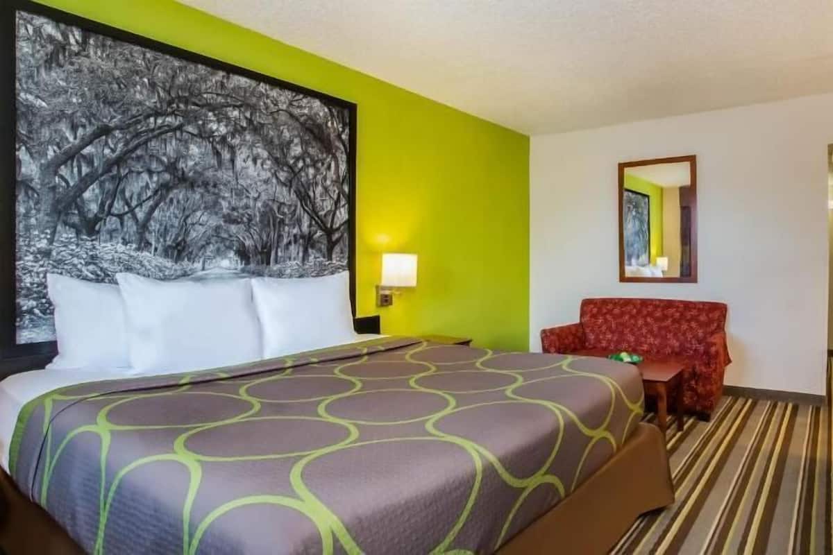 A hotel room with a bed, a desk, a chair, a mirror, and a painting on the wall.