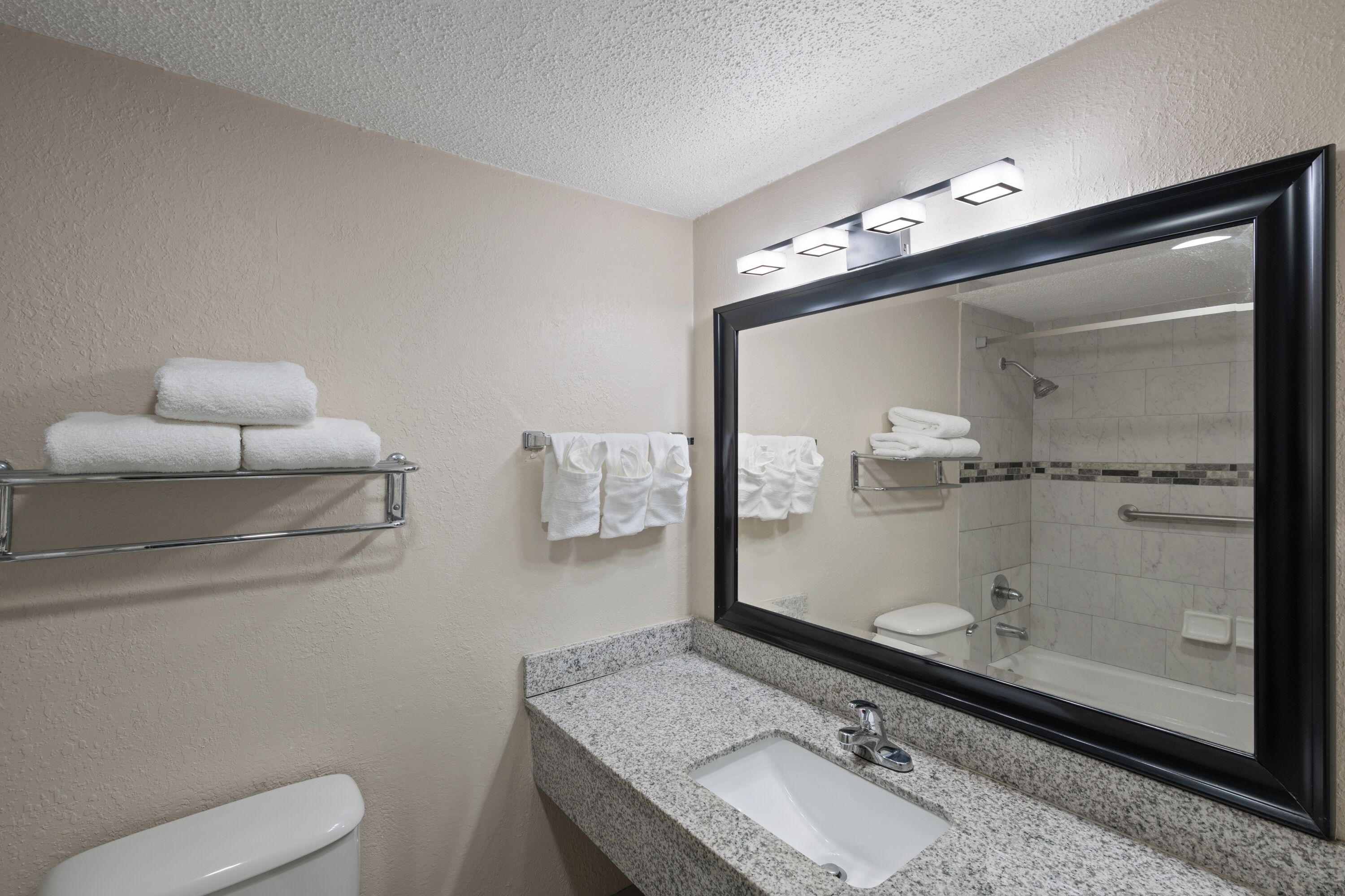 A bathroom with a granite countertop sink, a large mirror, and a shower stall.