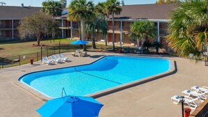 A swimming pool with lounge chairs and umbrellas, surrounded by a brick building with balconies and palm trees. - Super 8 by Wyndham Lake City (Lake City)