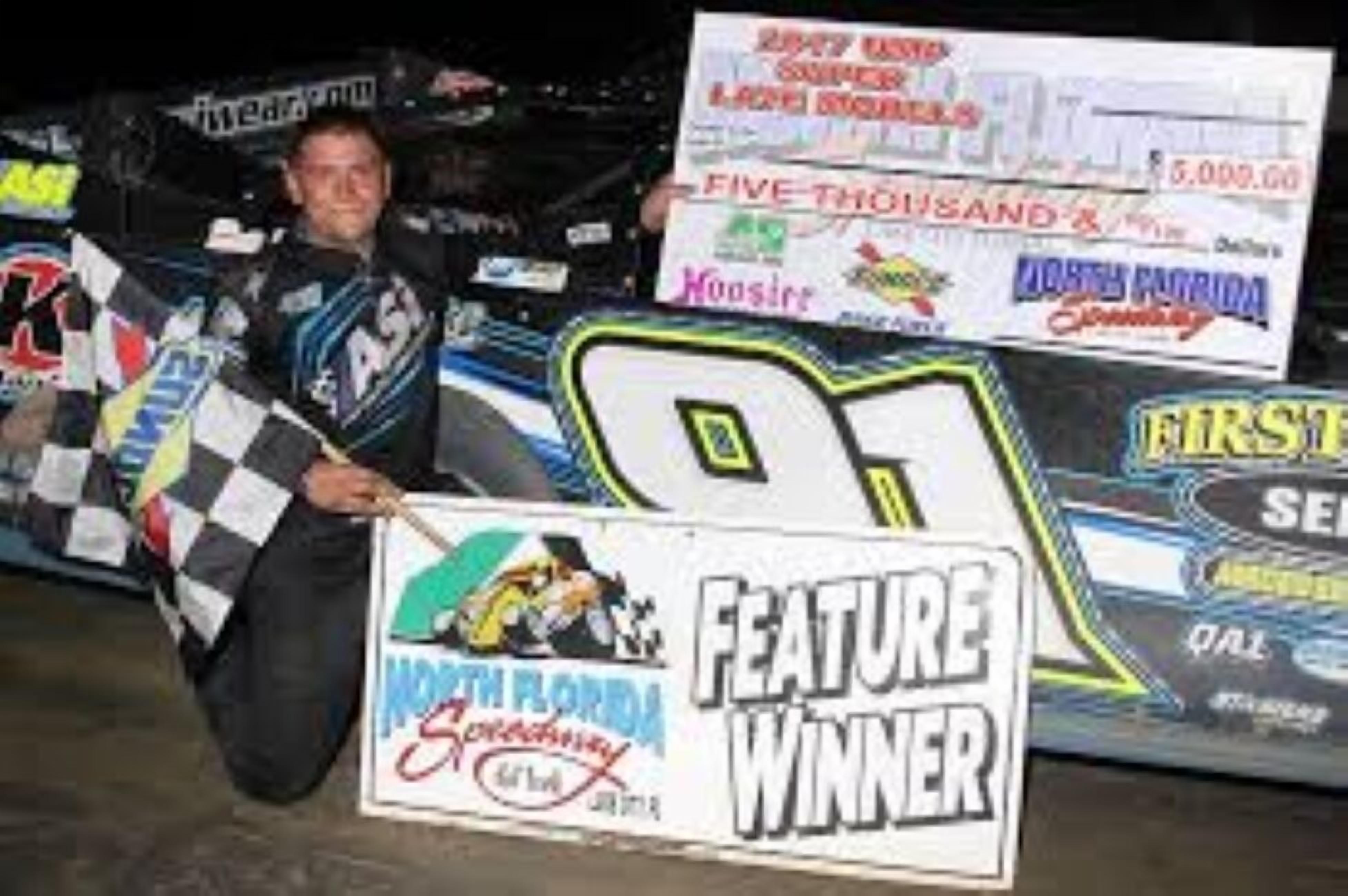 Eine Person hält ein Schild mit der Aufschrift 'FEATURE WINNER' und einen Scheck über 5.000 Dollar.