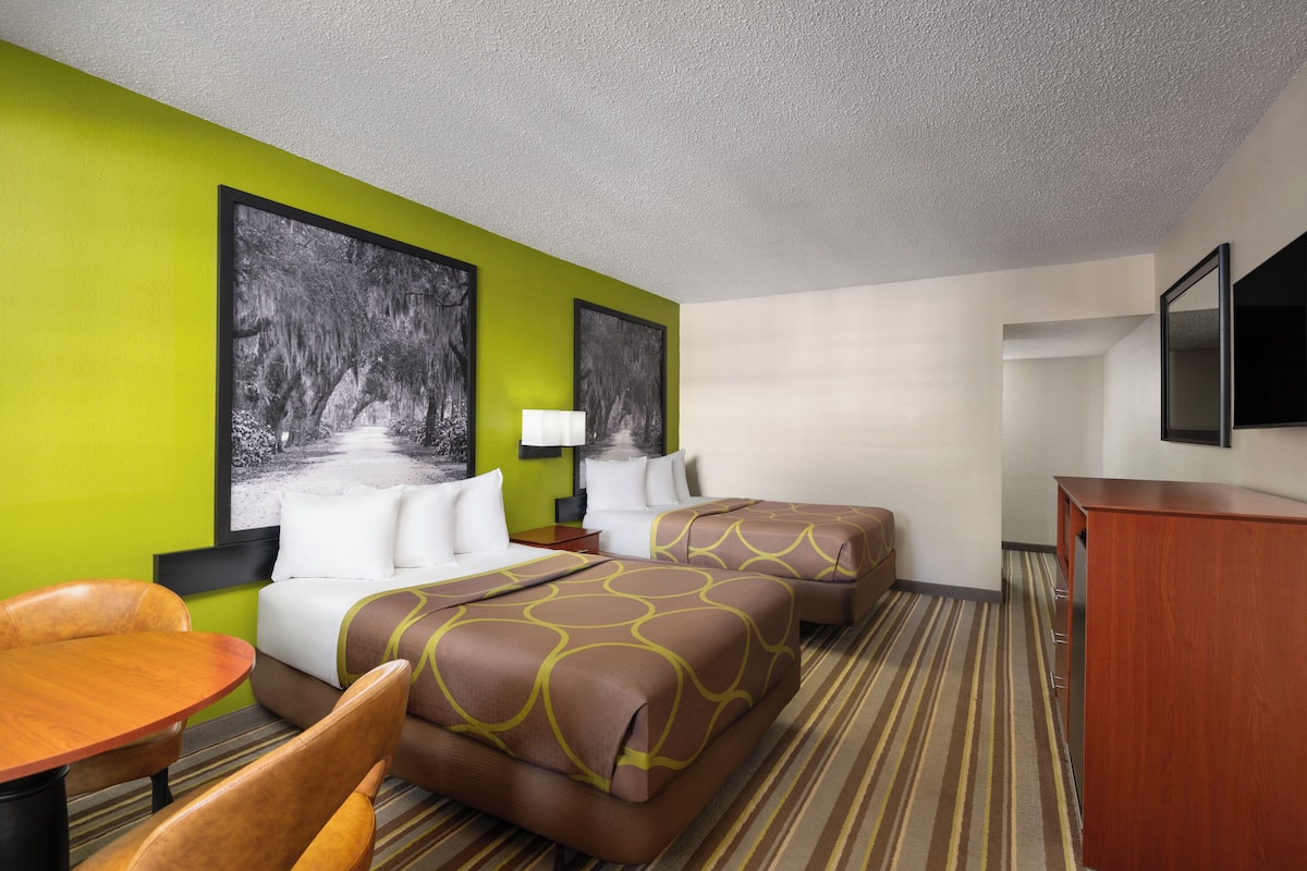 A hotel room with two beds, a desk, a chair, and a television.