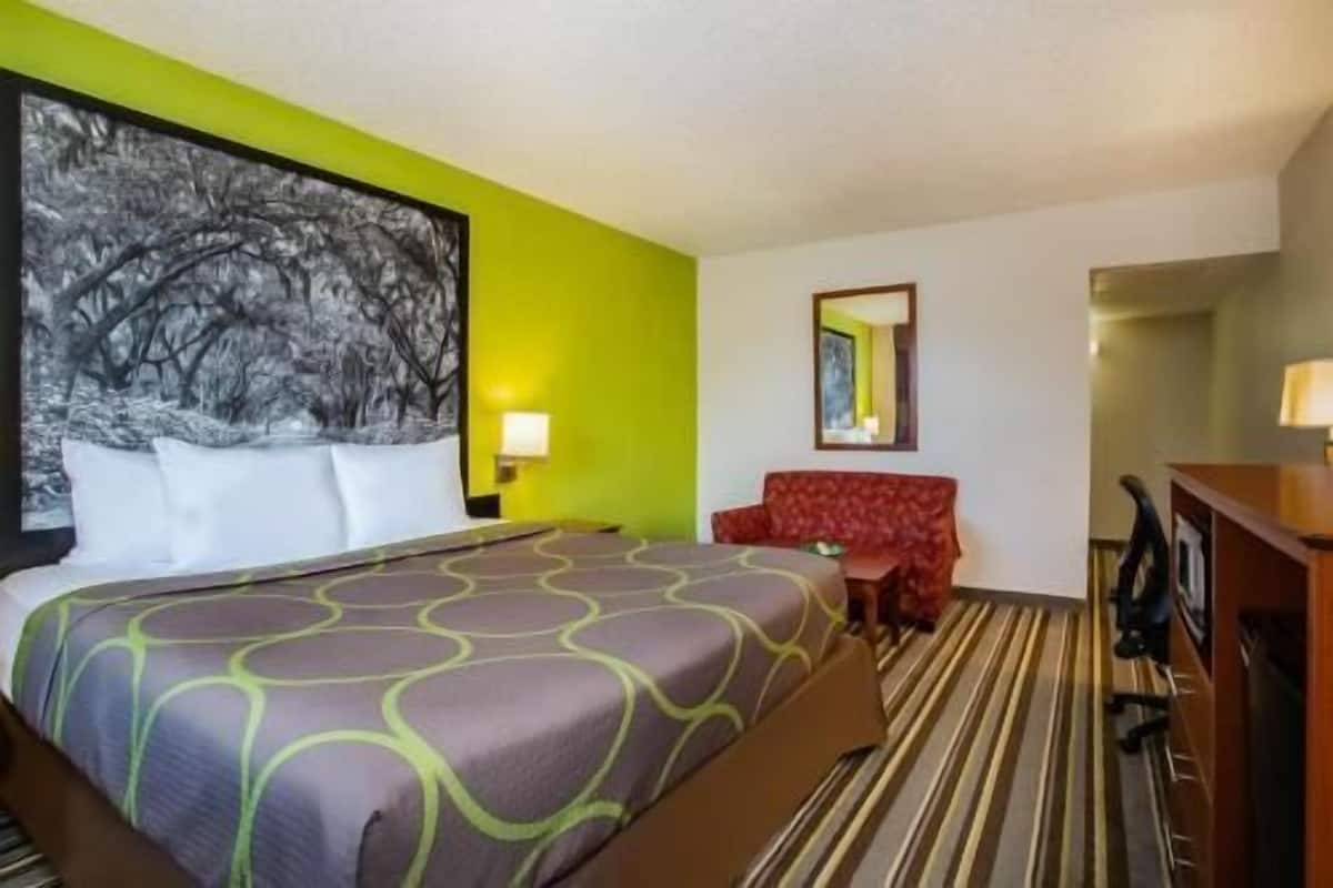 A hotel room with a bed, a red sofa, a desk, and a painting on the wall.