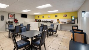 A restaurant with a yellow accent wall, white tiled floor, and black and blue chairs. - Super 8 by Wyndham Lake City (Lake City)