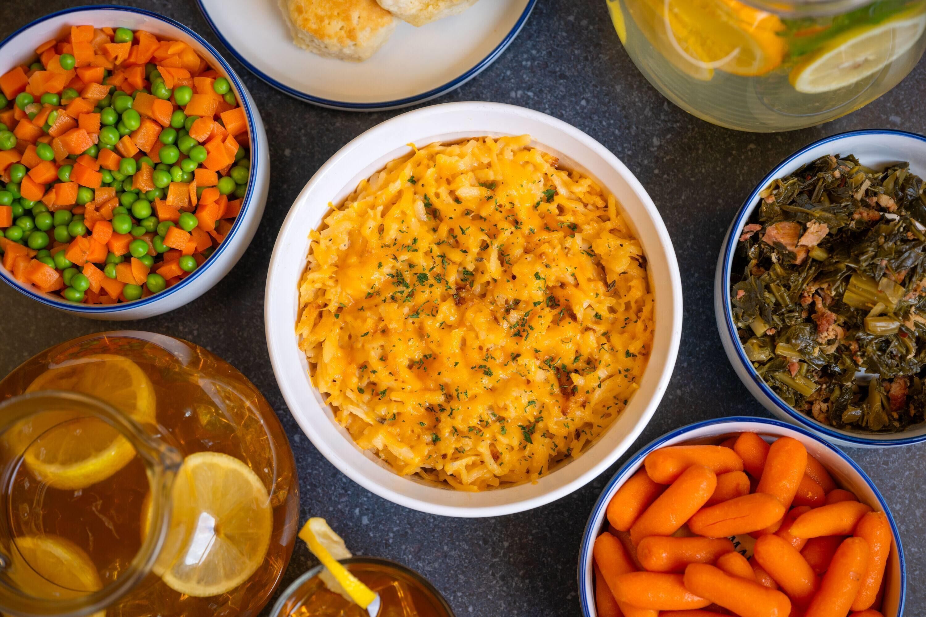 A table with various dishes including a bowl of pasta, a bowl of carrots, a bowl of greens, and a pitcher of lemonade.