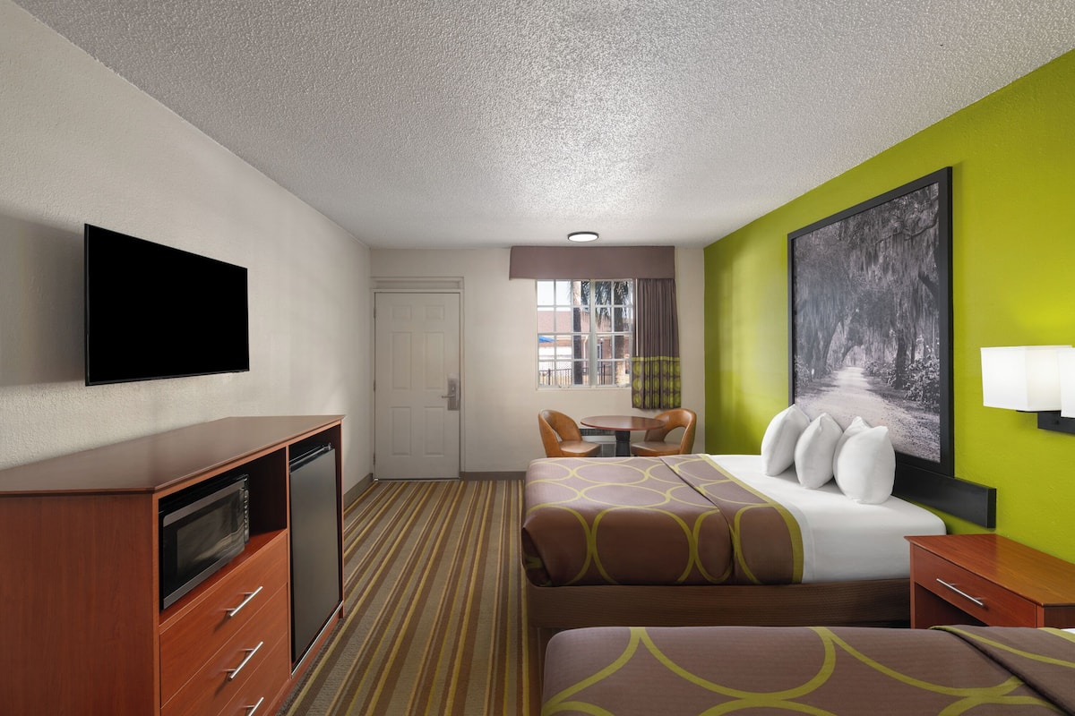 A hotel room with a bed, a desk, a television, a window, and a painting on the wall.