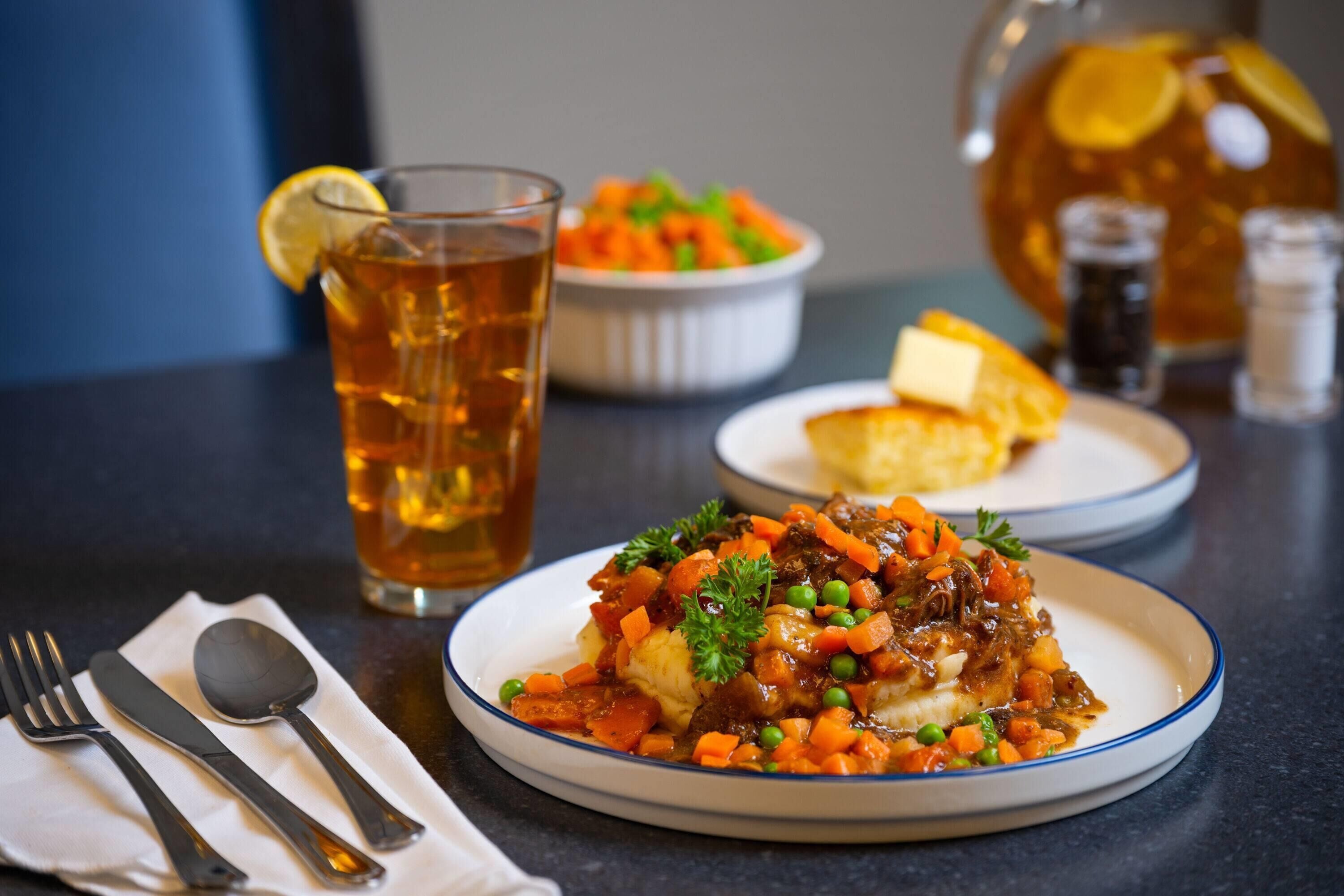 A plate of food with a glass of tea and a pitcher in the background.