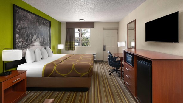 A hotel room with a large bed, a desk with a computer, a television, and a window with curtains. - Super 8 by Wyndham Lake City (Lake City)