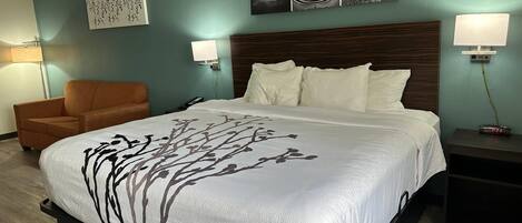 A hotel room with a large bed, a chair, a nightstand, and wall art.