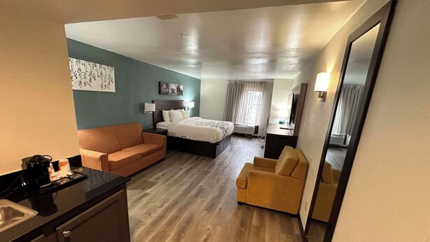 Hotellihuone, jossa on sänky, sohva, tuoli, työpöytä, kahvinkeitin ja peili.