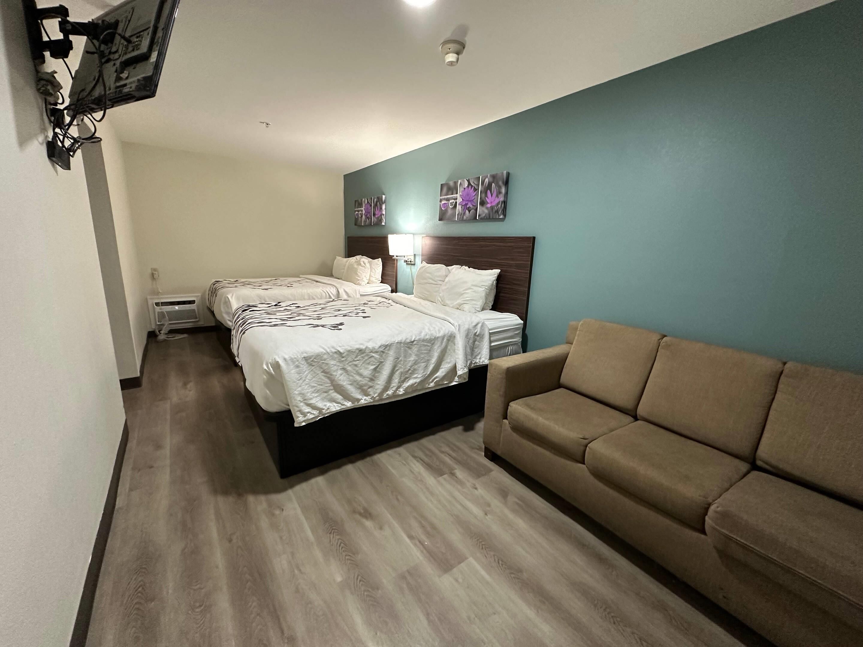 A hotel room with a bed, two bedside tables, a couch, and a wall-mounted TV.