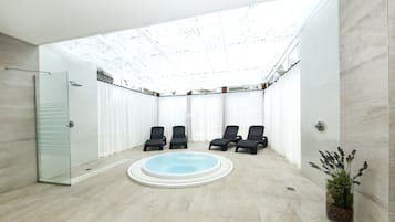 Un espace piscine intérieur moderne, doté d’un plafond en verre, d’une petite piscine et de quatre chaises longues.