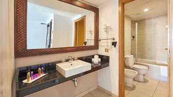 A bathroom with a large mirror, a sink, a toilet, and a shower area.